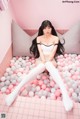 A woman sitting in a bathtub filled with pink and white balloons.